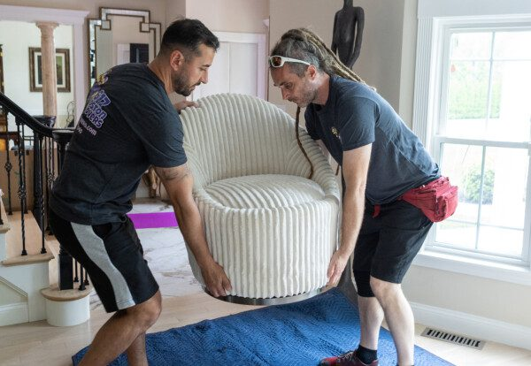 Two movers carrying a white armchair through a home
