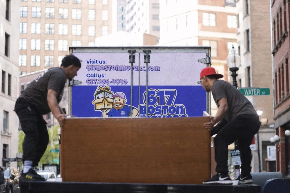 Two movers loading a wooden office desk into a truck in downtown Boston