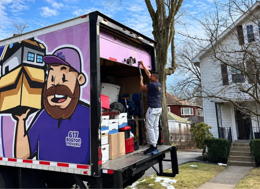 A 617 Boston Movers crew member loading equipment into the back of a moving truck in